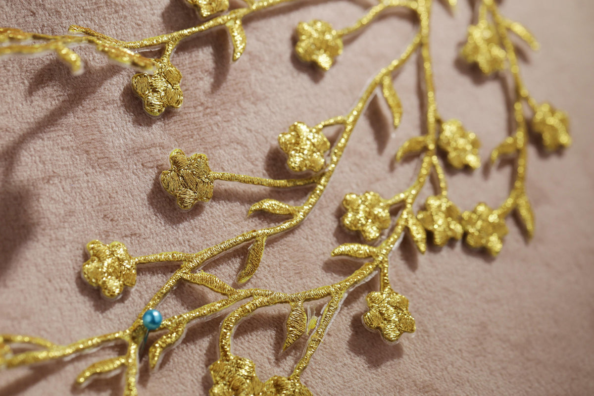 a close-up view of a delicate gold embroidered design on a pink fabric, with small gold flowers and leaves intricately arranged on the fabric.