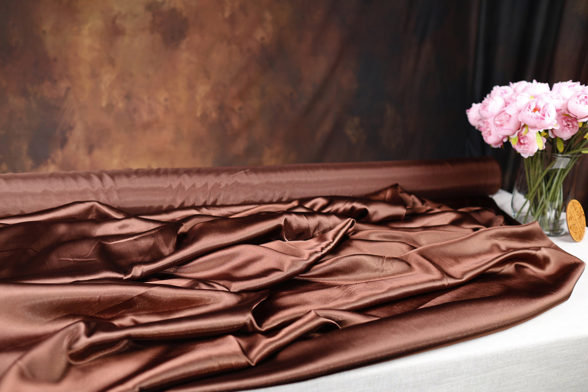 a close-up view of a brown satin fabric, with a vase of pink flowers placed next to it on a table.