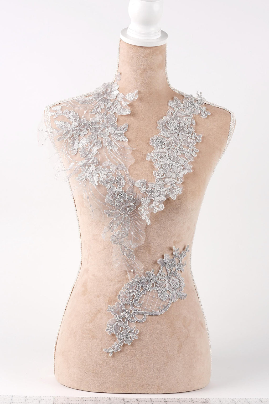 A mannequin wearing a beige dress with a delicate, intricate lace design on the neckline and shoulders.