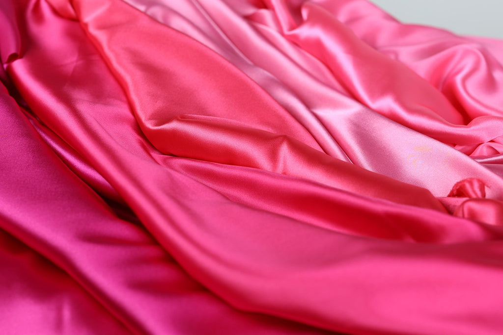 The image is a close-up of a fabric with a pink and red gradient, featuring a soft and flowing texture.