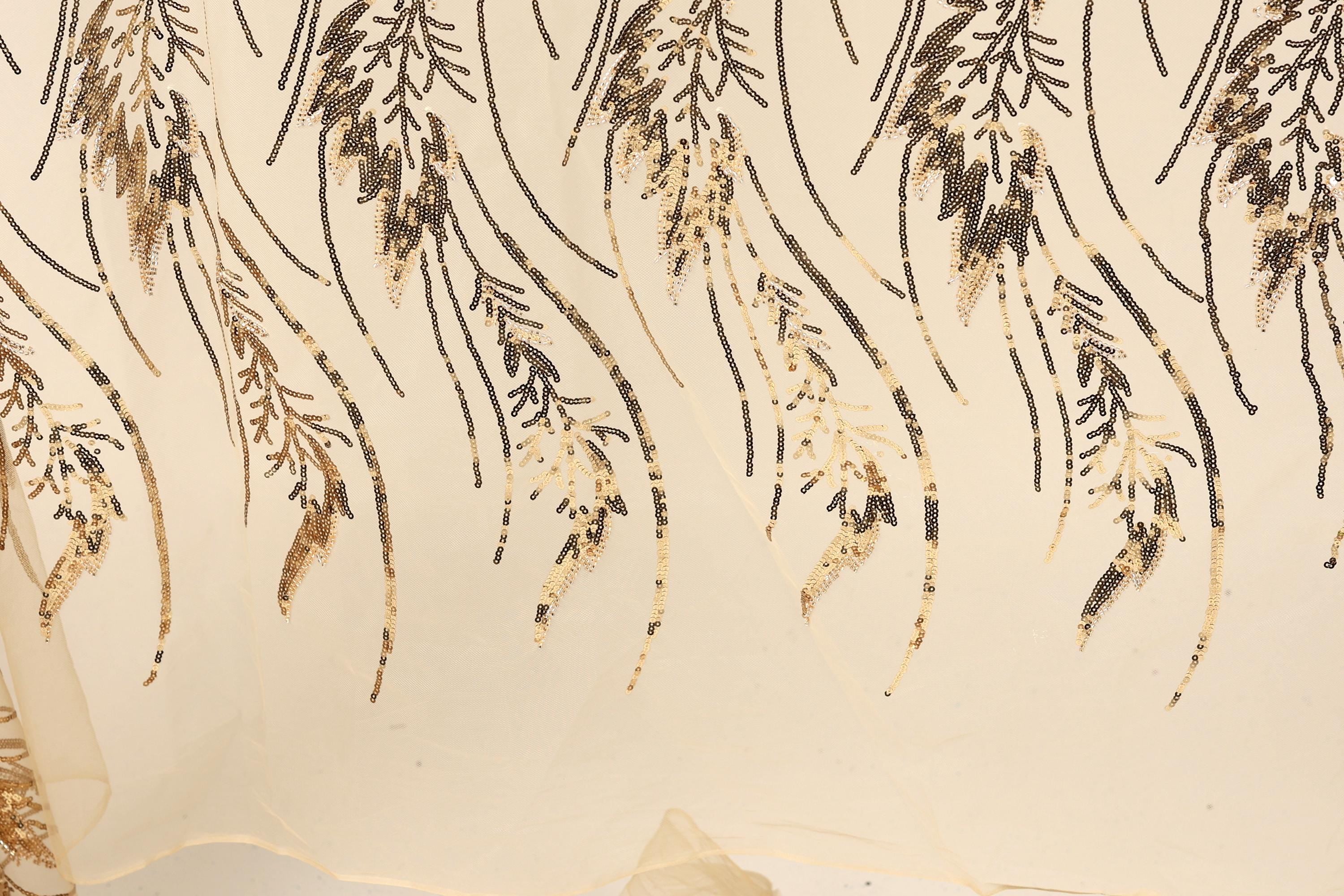 a close-up view of a fabric with a repeating pattern of gold and black sequin designs. The pattern consists of various shapes and lines, creating a visually striking and intricate design.