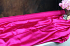 a close-up view of a vibrant pink satin fabric, with a vase of pink flowers placed next to it.