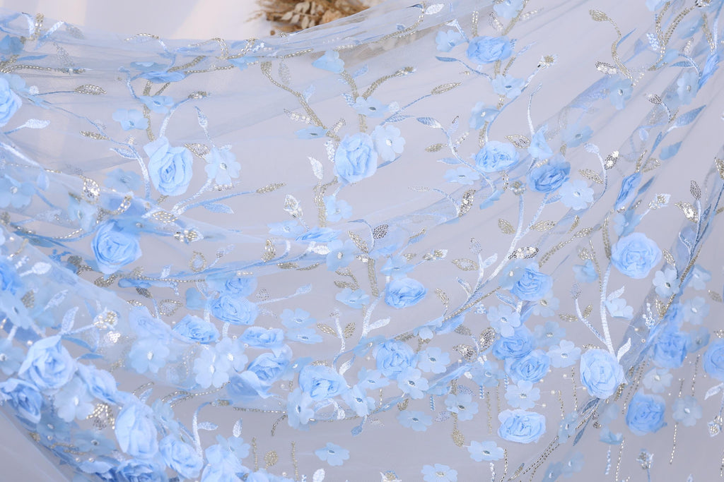 a close-up view of a delicate, light blue fabric adorned with a floral pattern of blue flowers and leaves. The fabric appears to be made of sheer material, giving it a soft and airy appearance. The intricate design and the delicate nature of the flowers and leaves create a visually appealing and elegant look.