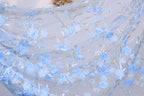 a close-up view of a delicate, light blue fabric adorned with a floral pattern of blue flowers and leaves. The fabric appears to be made of sheer material, giving it a soft and airy appearance. The intricate design and the delicate nature of the flowers and leaves create a visually appealing and elegant look.