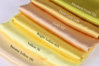 A stack of six fabric swatches in various shades of yellow, including mustard, gold, bright yellow, banana yellow, and bright yellow.
