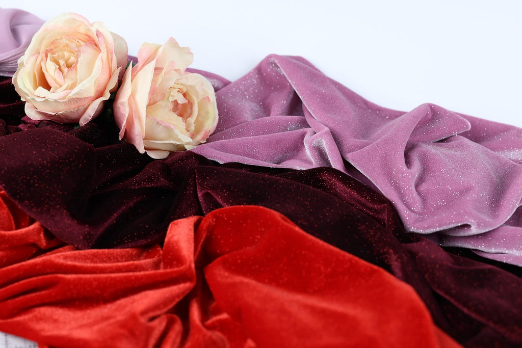 a close-up view of two delicate pink roses resting on a bed of red and purple velvet fabric.