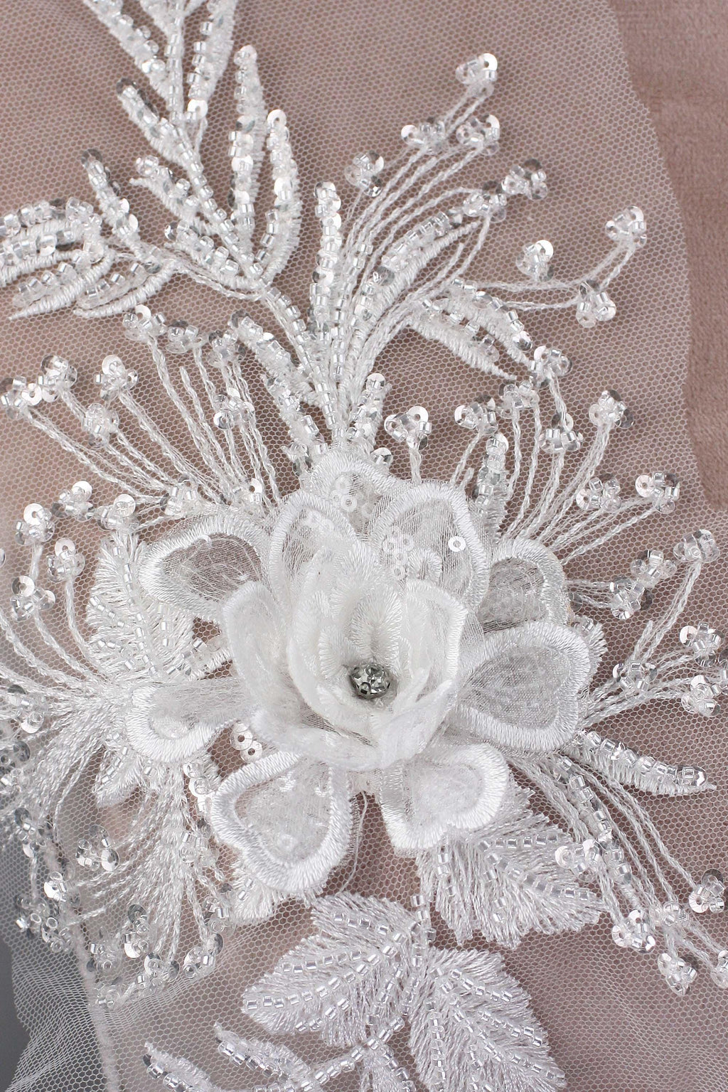 The image is a close-up of a delicate white lace flower with a small gemstone in the center, surrounded by intricate white lace patterns and sequins.