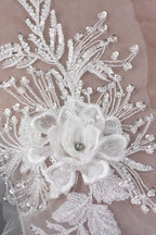 The image is a close-up of a delicate white lace flower with a small gemstone in the center, surrounded by intricate white lace patterns and sequins.