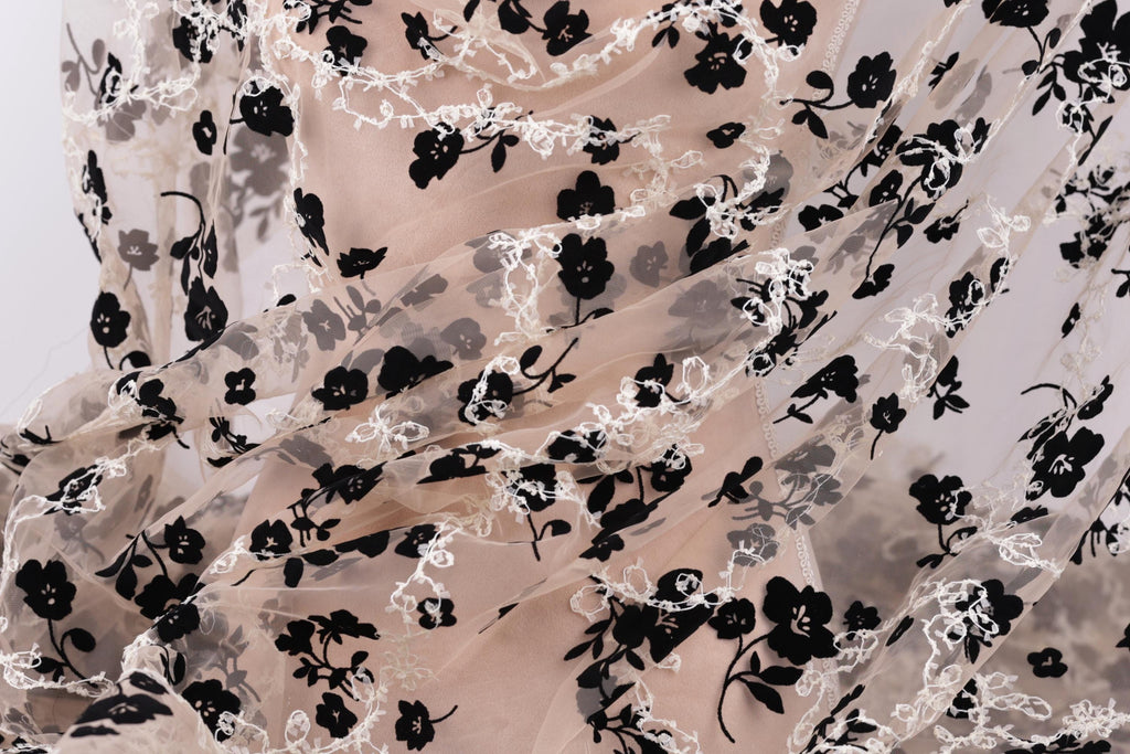 a close-up view of a fabric with a floral pattern, featuring black and white flowers and leaves. The fabric appears to be made of sheer material, giving it a delicate and airy appearance.