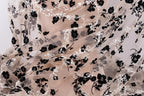 a close-up view of a fabric with a floral pattern, featuring black and white flowers and leaves. The fabric appears to be made of sheer material, giving it a delicate and airy appearance.
