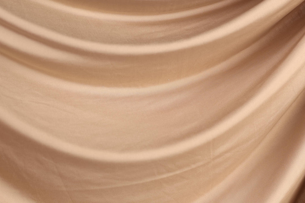 The image is a close-up of a light brown fabric, possibly a piece of clothing or a textile. The fabric has a smooth, flowing texture and appears to be made of a soft, shiny material.