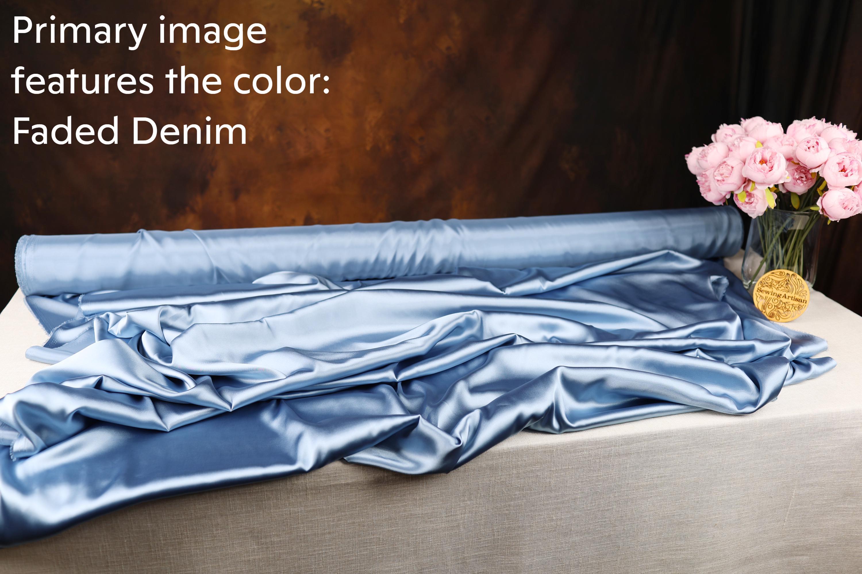 a roll of blue satin fabric with a faded denim texture, placed on a table next to a vase filled with pink flowers.