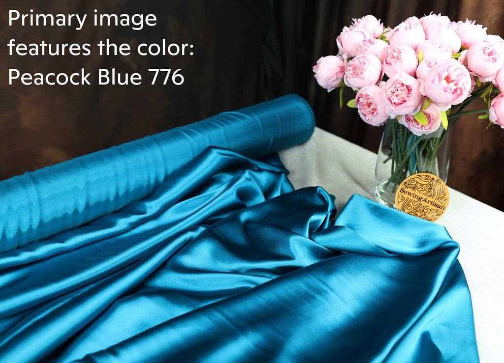 a roll of blue satin fabric and a vase of pink peonies on a table.
