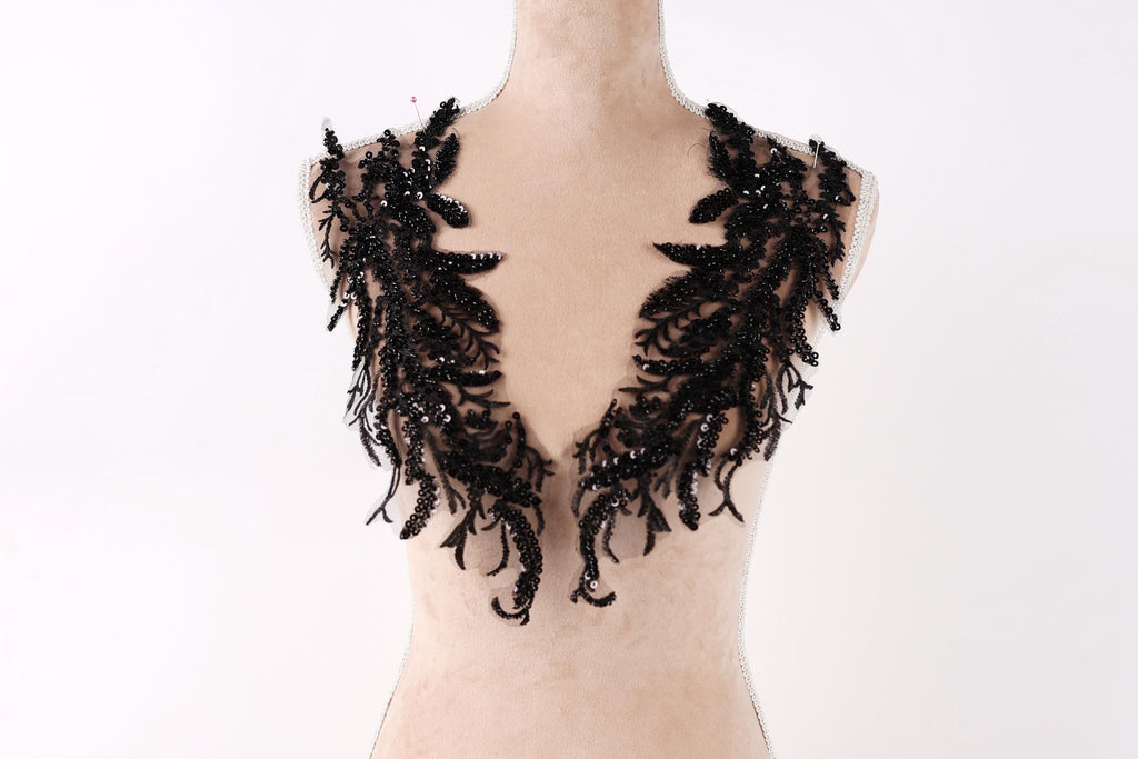 A mannequin wearing a black lace neck piece with intricate, flowing patterns.