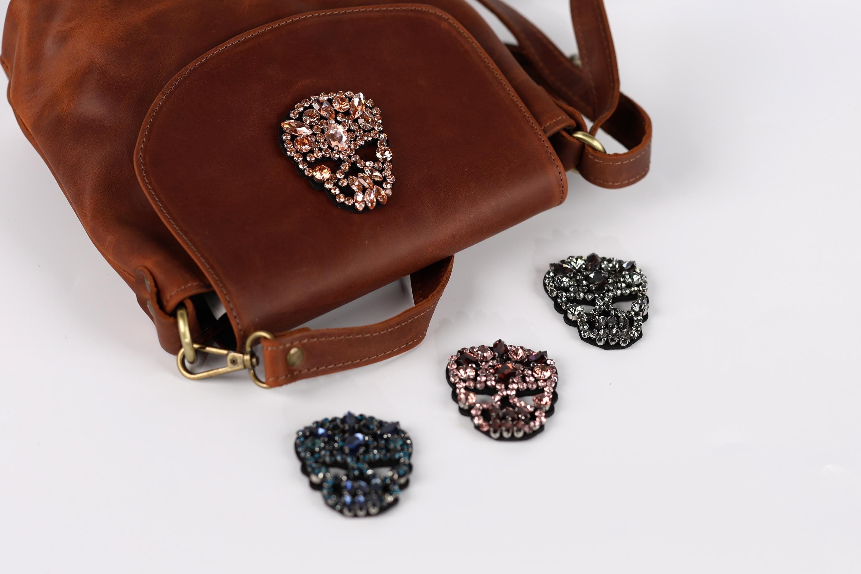 A brown leather handbag with a skull-shaped embellishment on it, along with four small skull-shaped charms in various colors.