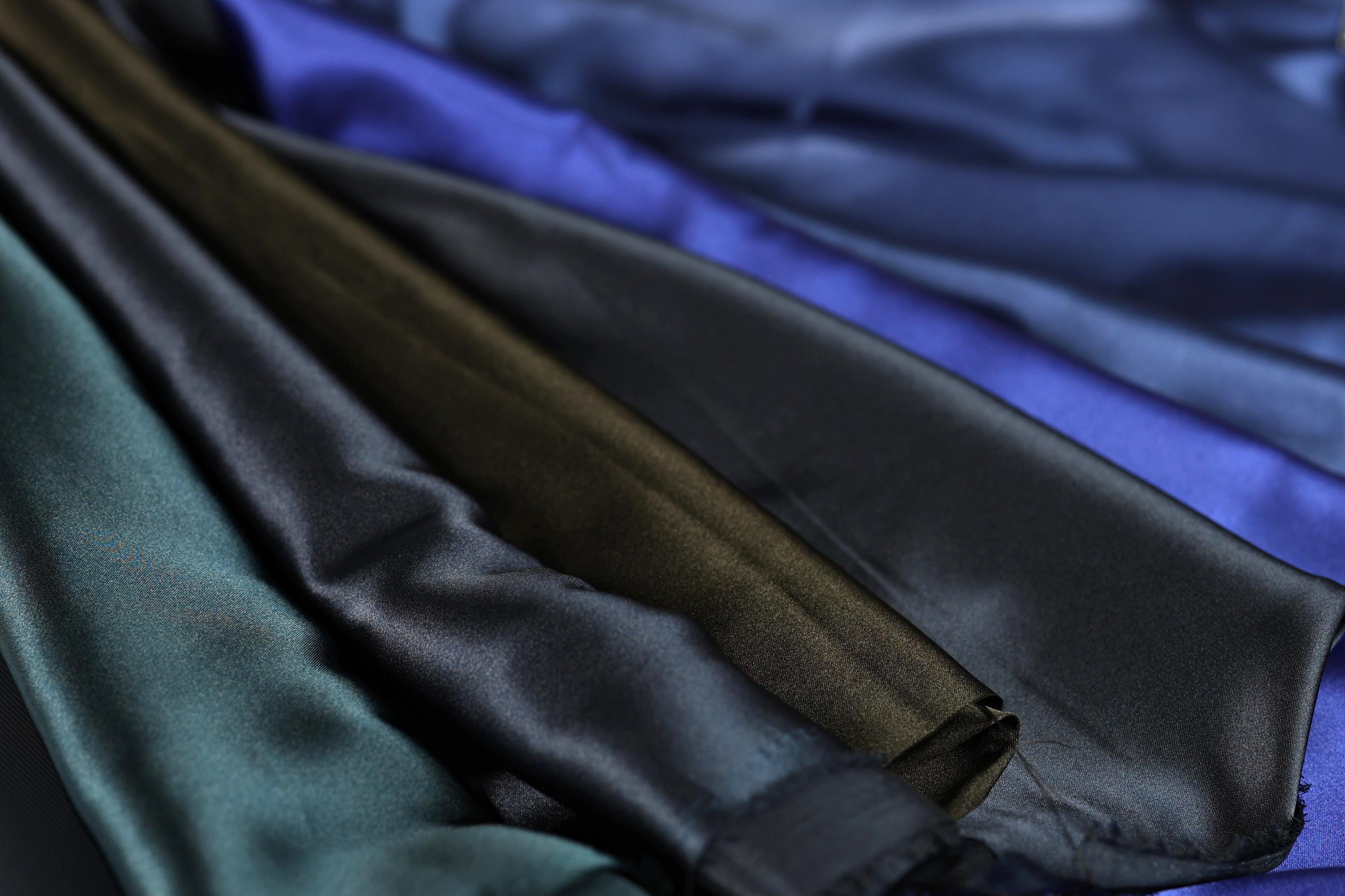 A close-up view of various colored satin fabric, including shades of blue, green, and brown.