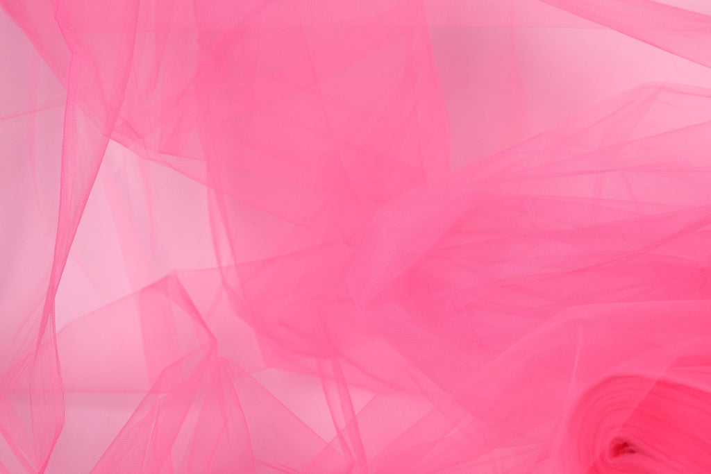 The image is a close-up of a pink fabric, possibly tulle, with a soft, flowing texture. The fabric appears to be slightly wrinkled, giving it a delicate and delicate appearance.