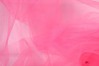 The image is a close-up of a pink fabric, possibly tulle, with a soft, flowing texture. The fabric appears to be slightly wrinkled, giving it a delicate and delicate appearance.
