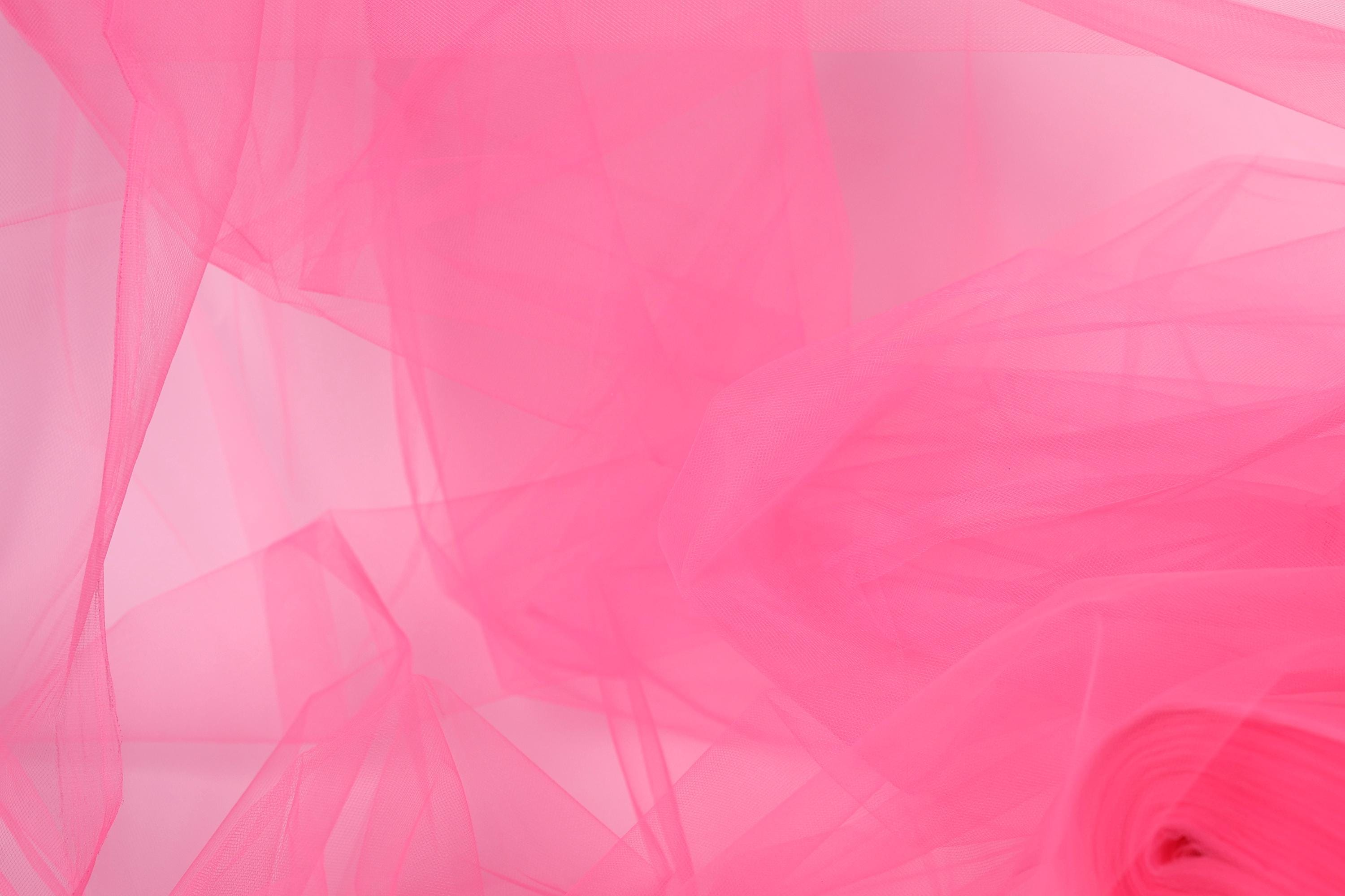 The image is a close-up of a pink fabric, possibly tulle, with a soft, flowing texture. The fabric appears to be slightly wrinkled, giving it a delicate and delicate appearance.