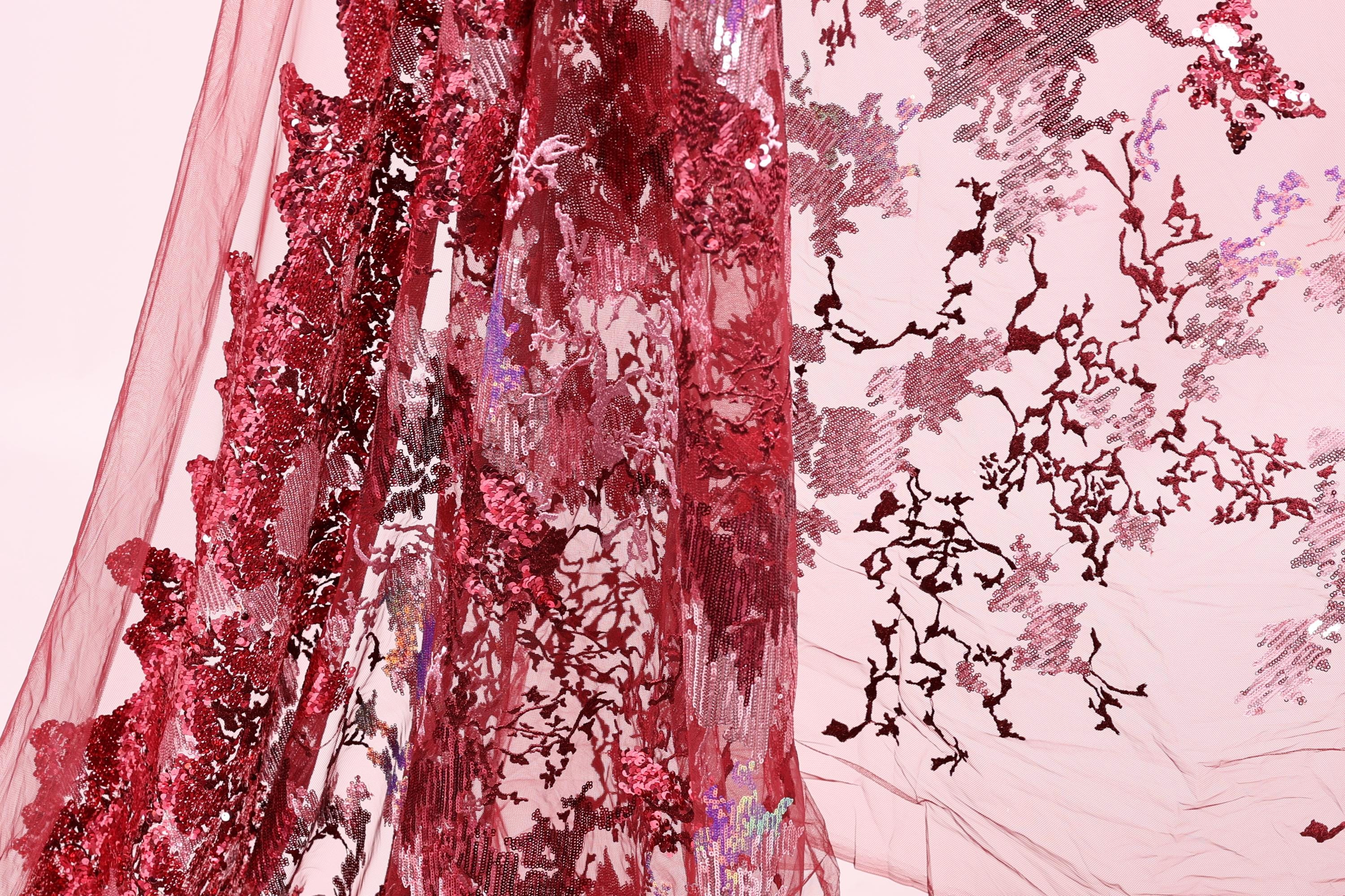 a close-up view of a red fabric with a floral pattern, including red sequins and a pink background.