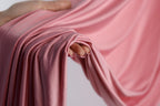 A hand is holding a pink fabric, with the fabric partially draped over the hand and the hand's fingers visible.