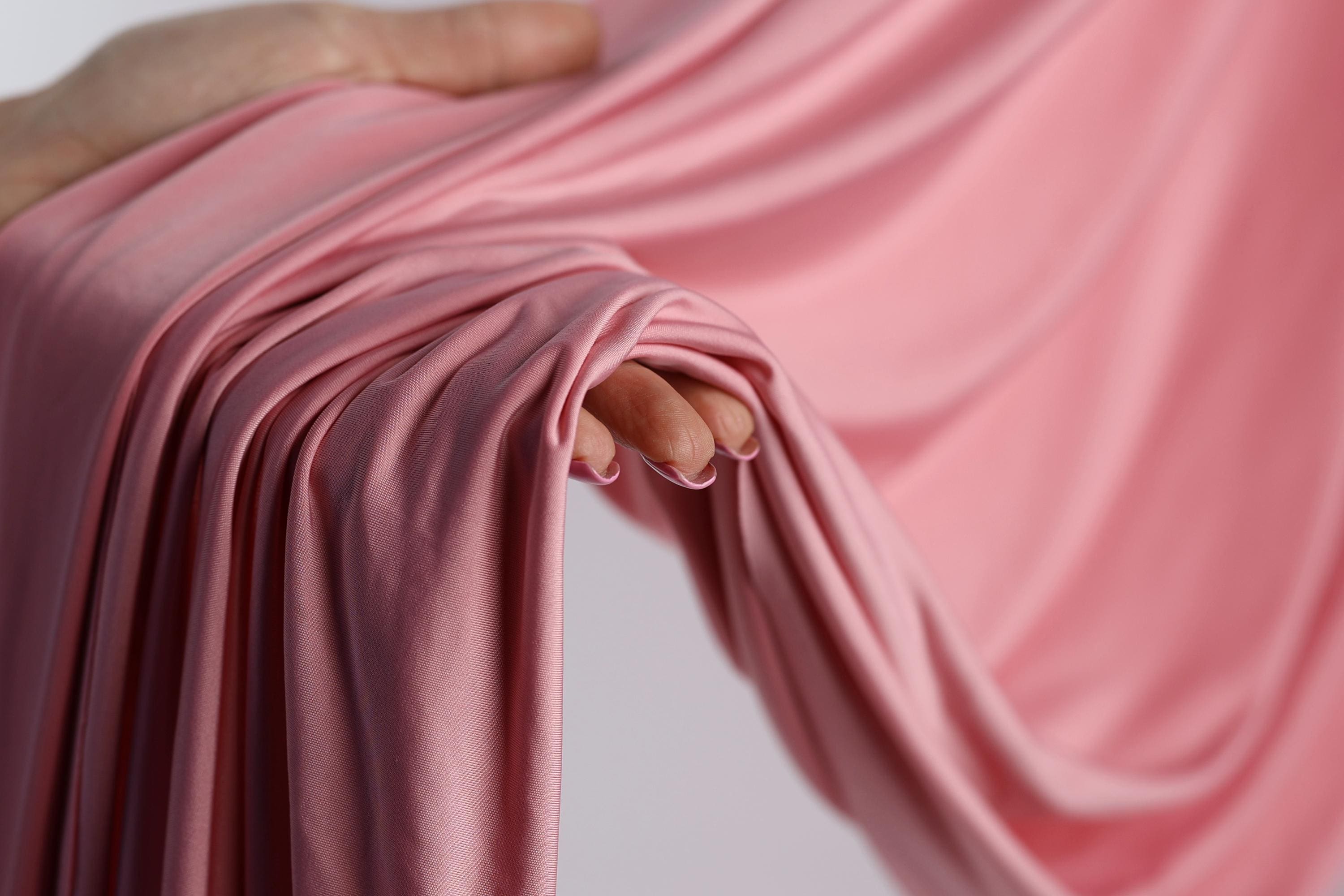A hand is holding a pink fabric, with the fabric partially draped over the hand and the hand's fingers visible.