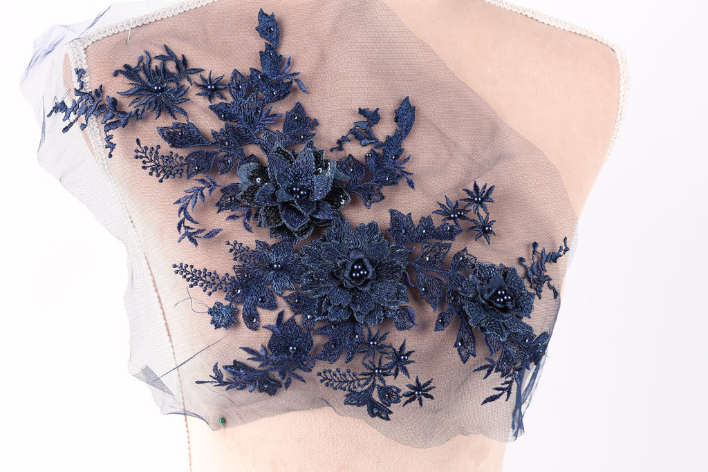 a close-up view of a delicate, intricate piece of blue lace or fabric adorned with a floral pattern. The lace features a variety of flowers and leaves, creating a visually appealing and detailed design. The fabric appears to be a light-colored material, possibly a sheer or sheer lace, which adds a delicate and ethereal touch to the overall appearance.