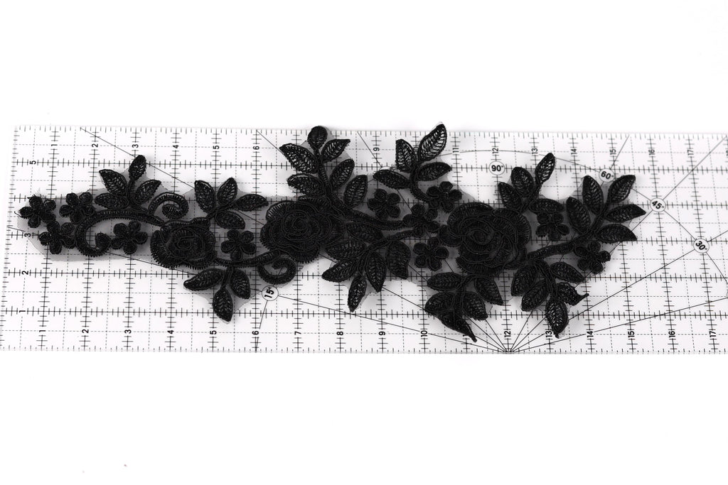 a black lace design with intricate floral patterns, including roses and leaves, arranged on a ruler for scale.
