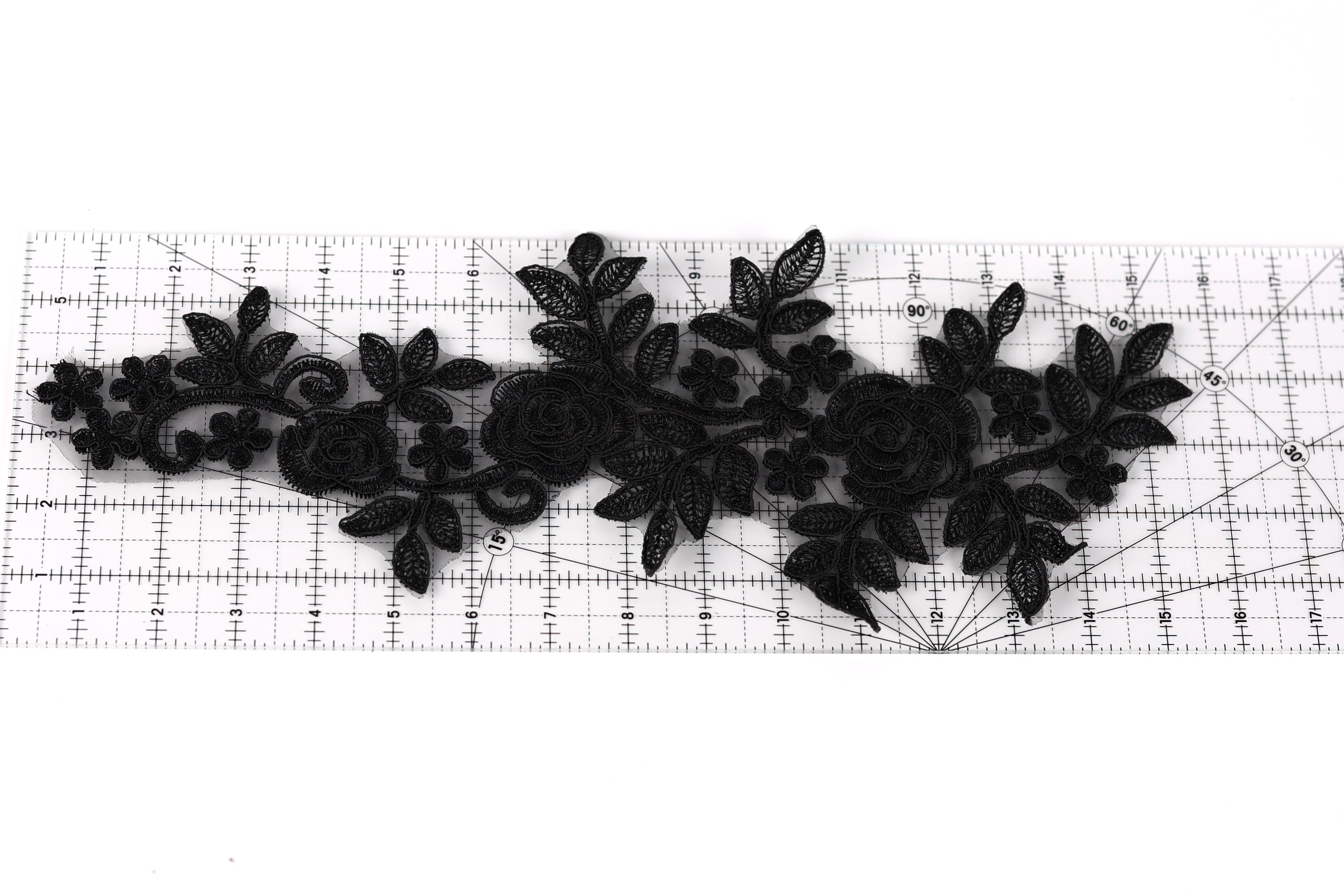 a black lace design with intricate floral patterns, including roses and leaves, arranged on a ruler for scale.