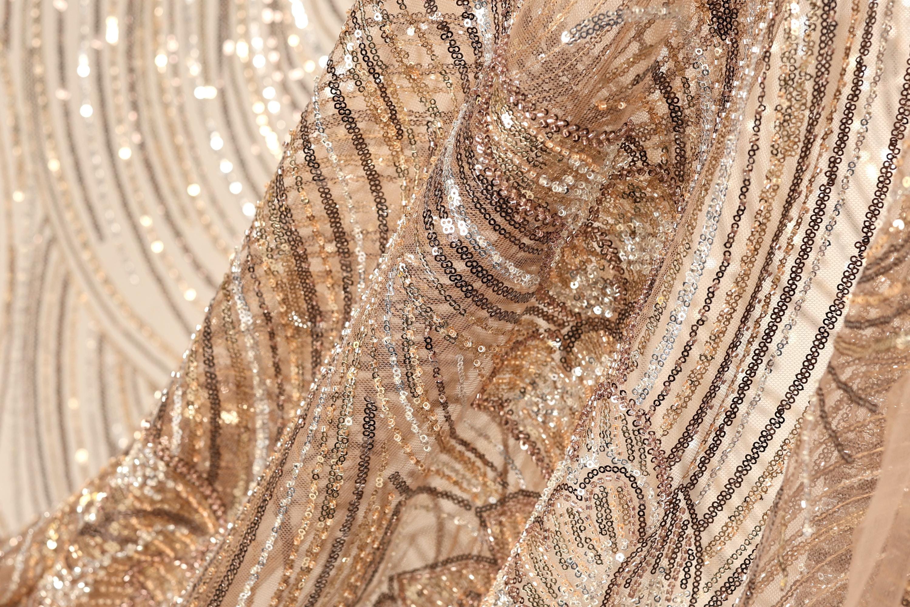 The image is a close-up of a fabric with a gold and black sequined pattern, featuring a mix of shimmering and metallic textures.