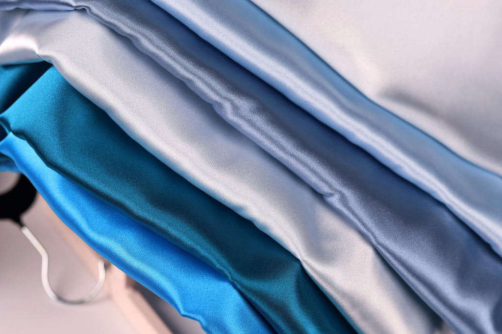 A close-up view of a pile of various colored satin fabric, including shades of blue, gray, and white.