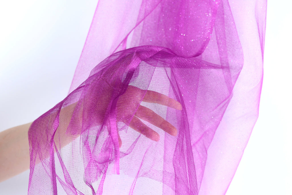 A hand is holding a piece of purple fabric, which appears to be a sheer or sheer-like material.