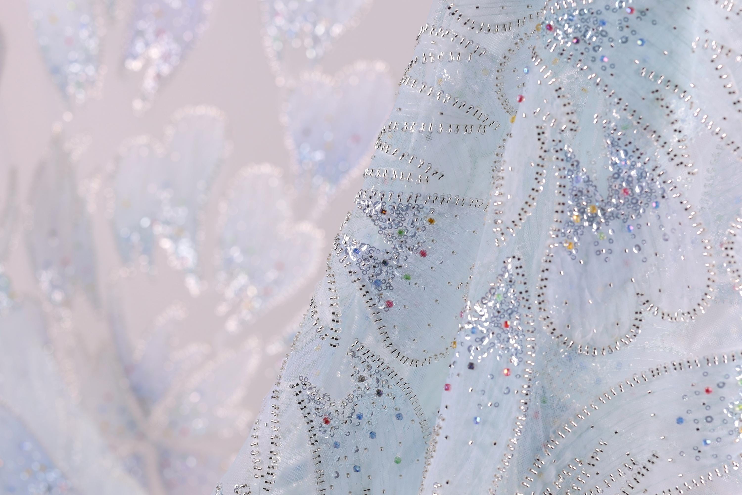 a close-up view of a fabric with a delicate, intricate pattern of silver and blue sequins or beads, creating a sparkling and shimmering effect.