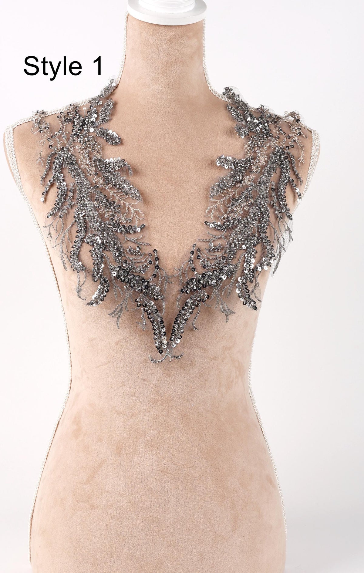 A mannequin wearing a beige dress with a decorative silver and black embellished neckline.