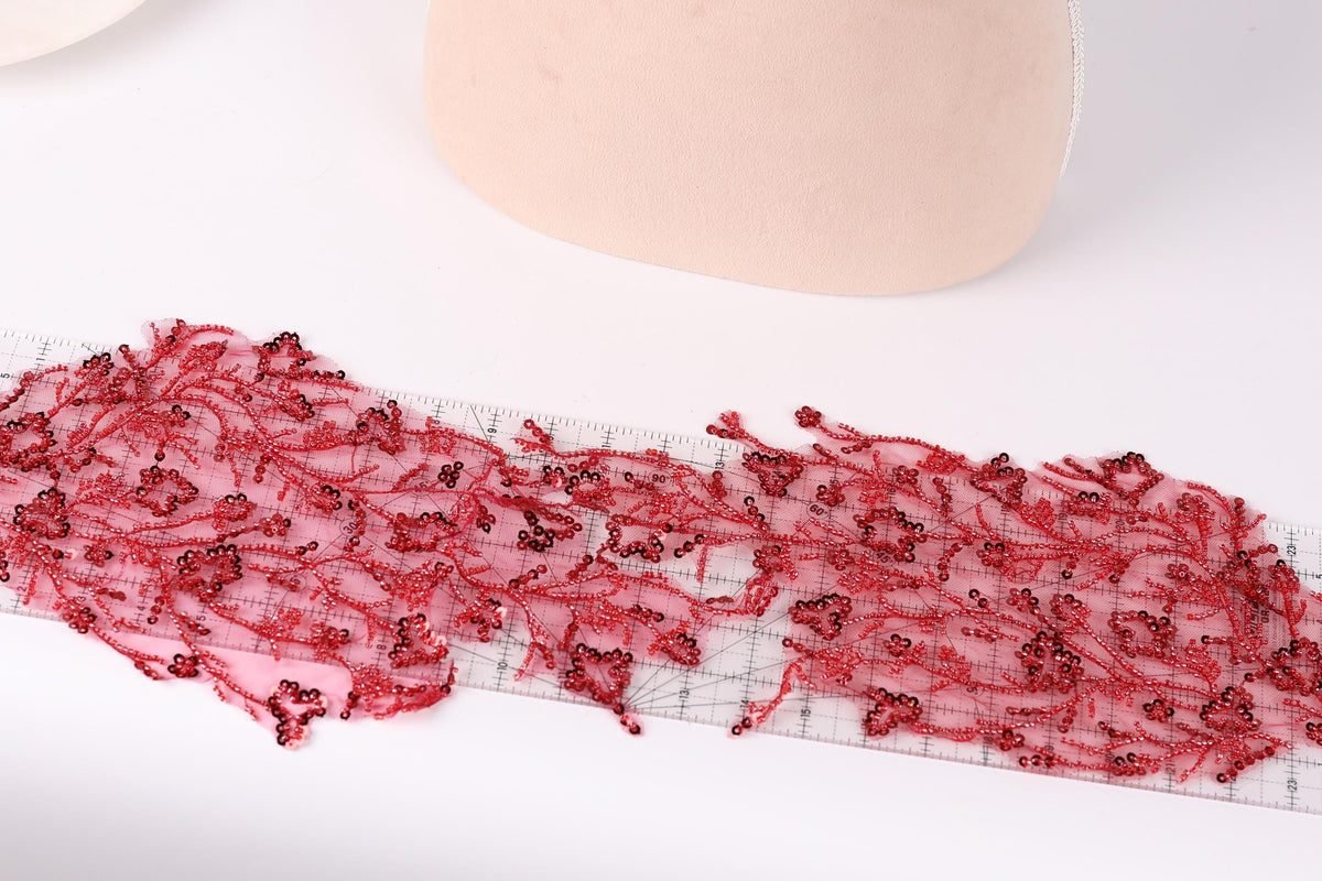 a close-up view of a piece of red lace with a floral pattern, placed on a white surface. There is a ruler visible in the background, suggesting that the lace may be part of a sewing or crafting project.