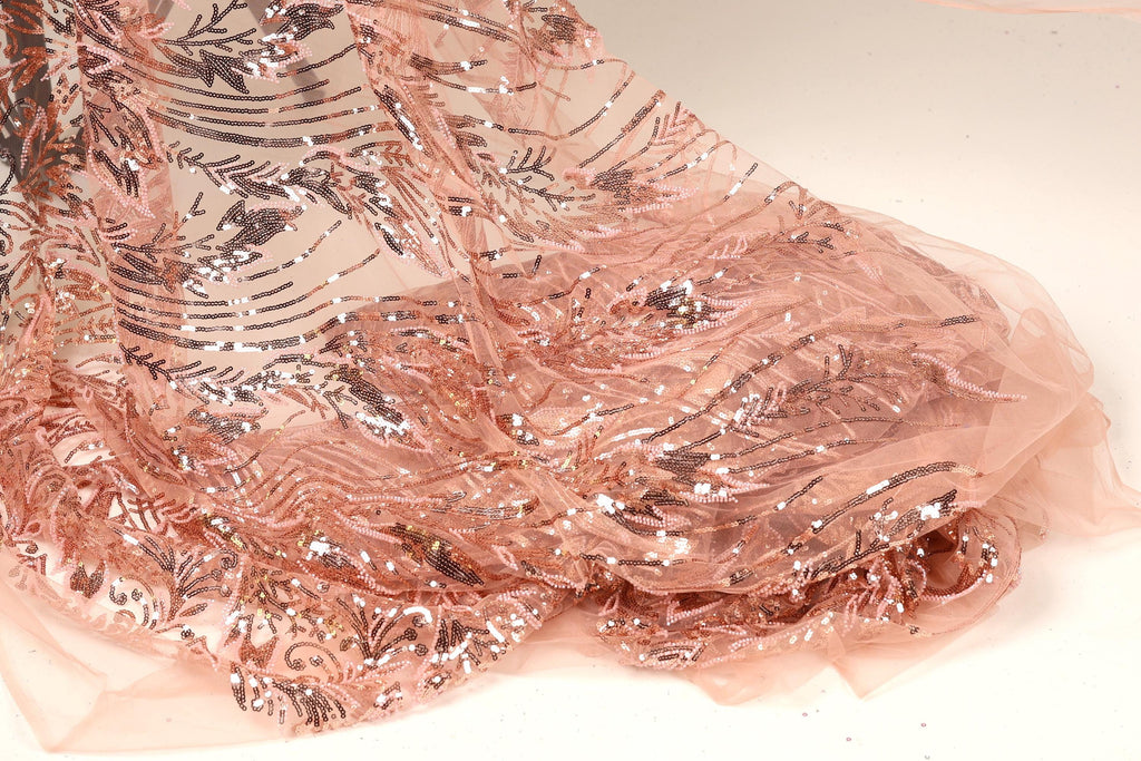a close-up view of a delicate, peach-colored fabric with a shimmering, sequined pattern. The fabric appears to be made of sheer material, giving it a delicate and elegant appearance.