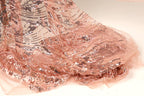 a close-up view of a delicate, peach-colored fabric with a shimmering, sequined pattern. The fabric appears to be made of sheer material, giving it a delicate and elegant appearance.