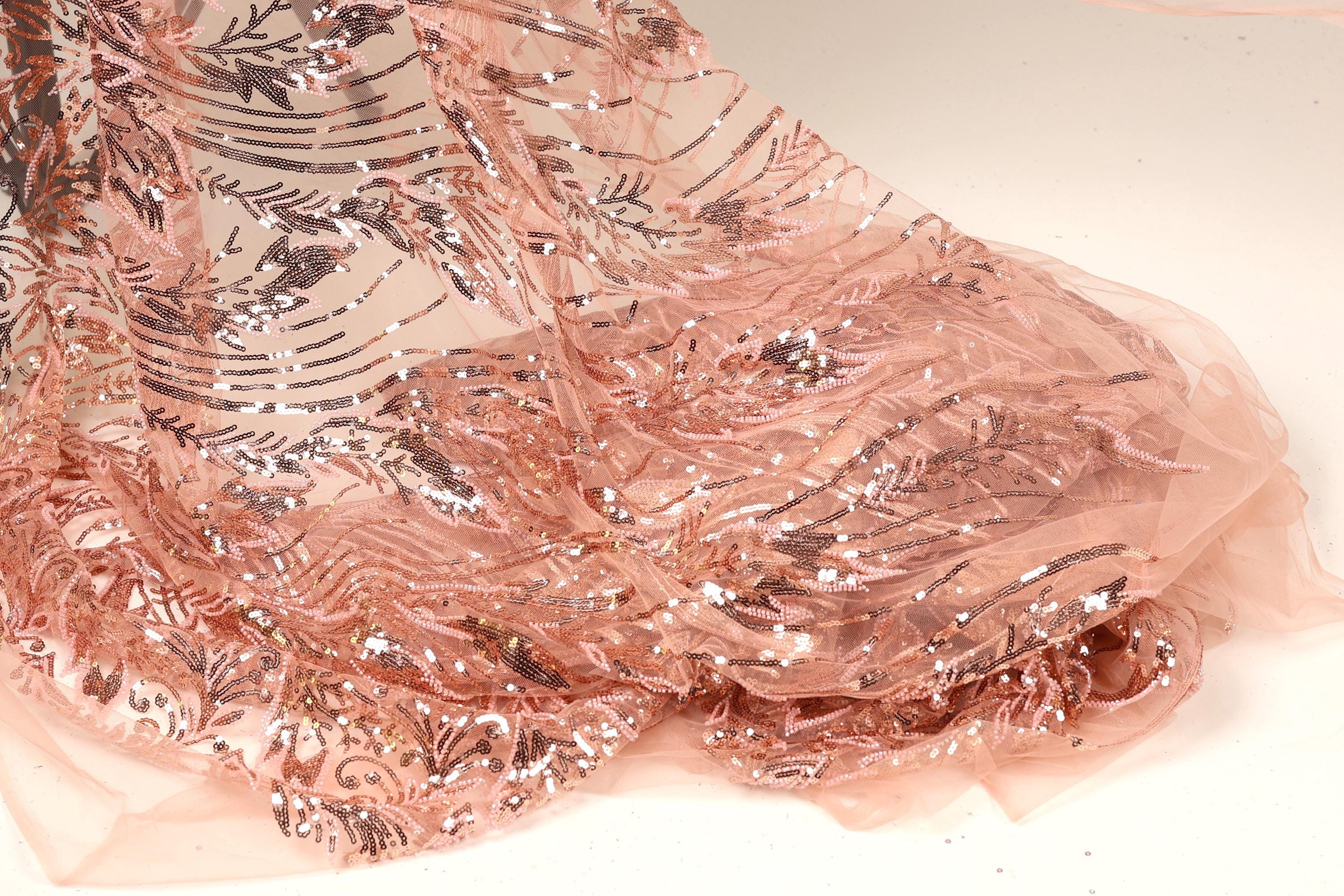 a close-up view of a delicate, peach-colored fabric with a shimmering, sequined pattern. The fabric appears to be made of sheer material, giving it a delicate and elegant appearance.