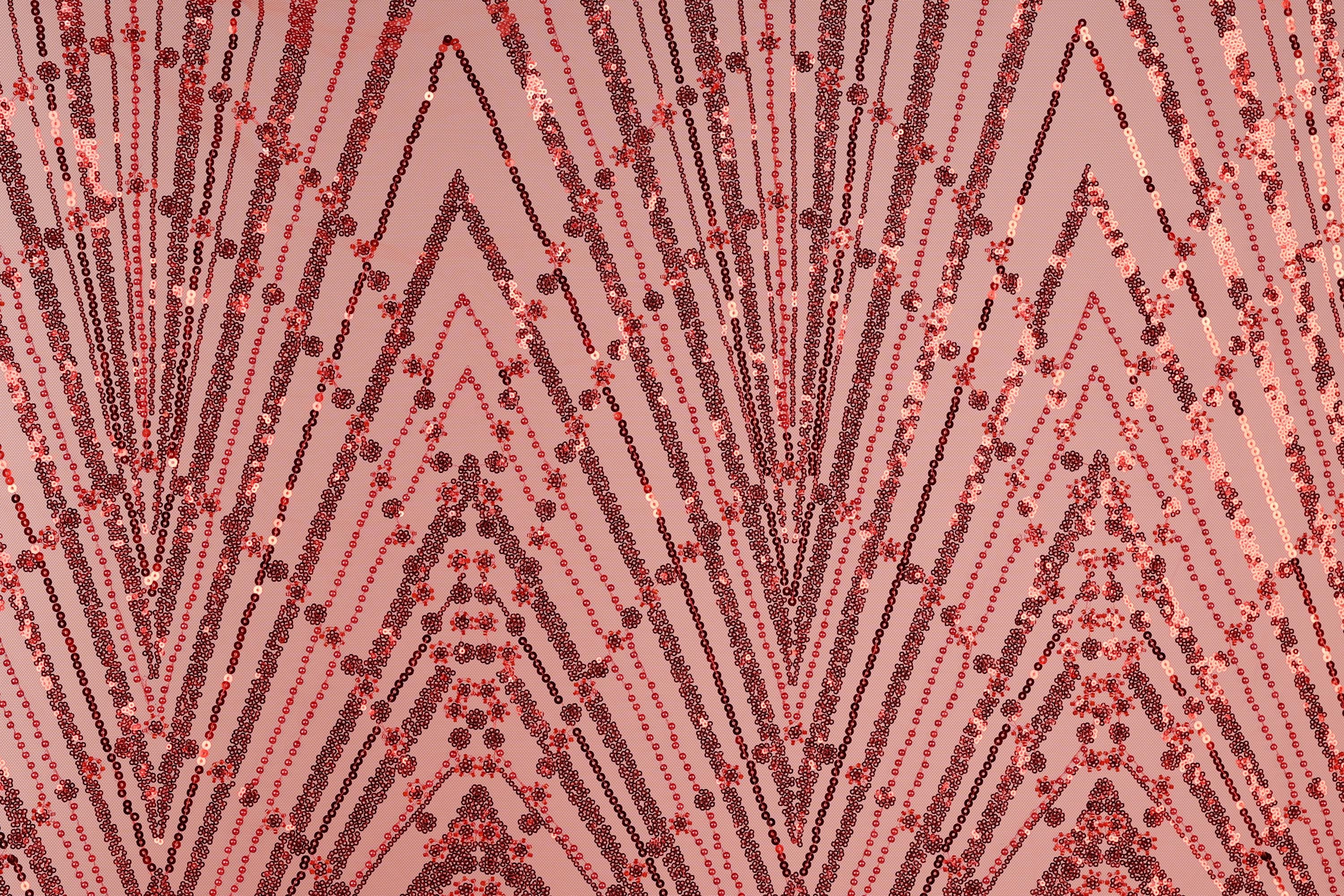 a close-up view of a fabric with a repeating pattern of red and black sequin designs. The pattern consists of diagonal lines and shapes, creating a visually striking and intricate design.