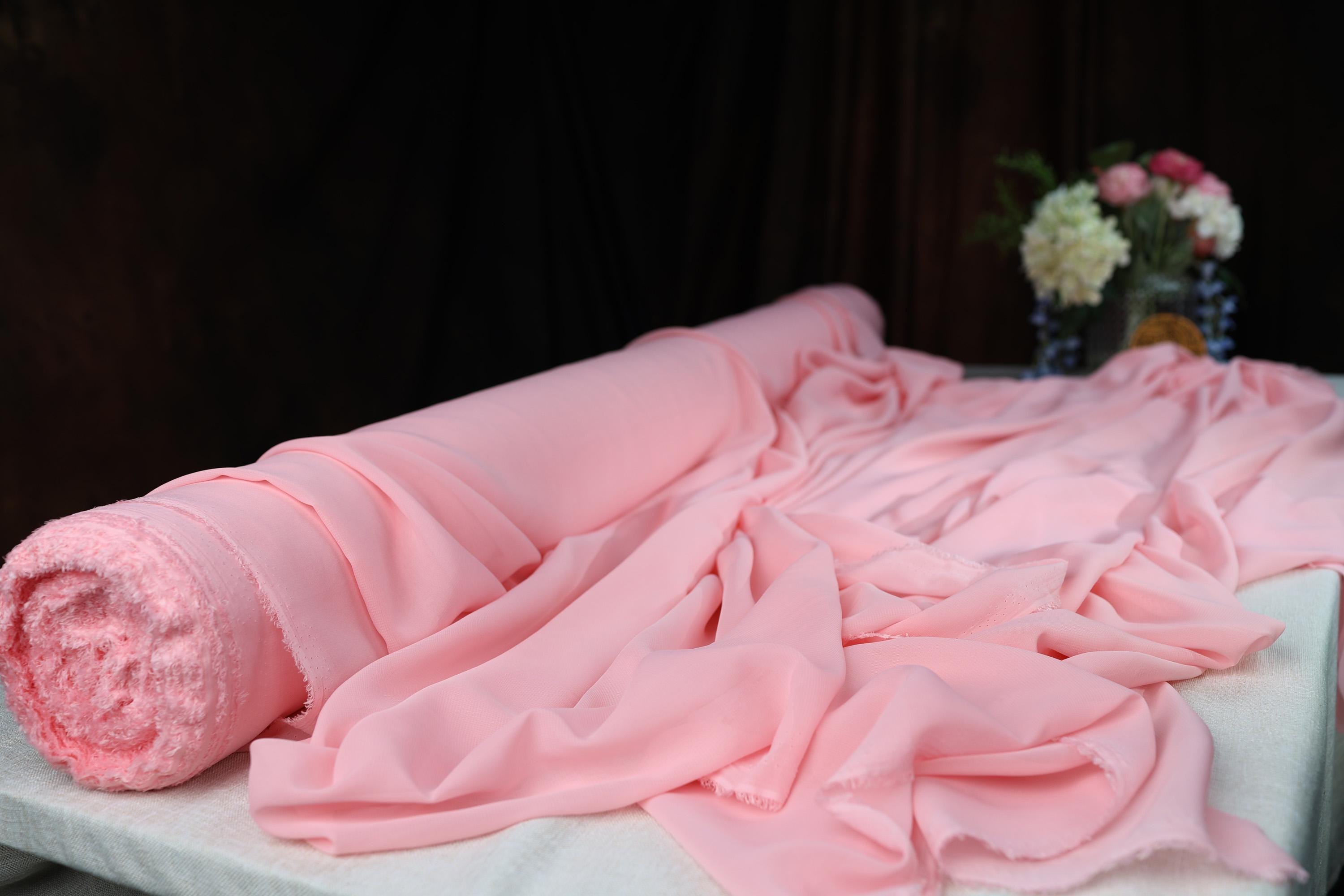 a pink blanket laying on top of a bed next to a vase of flowers