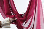 A hand is holding a red fabric, possibly a scarf or a garment, against a white background.