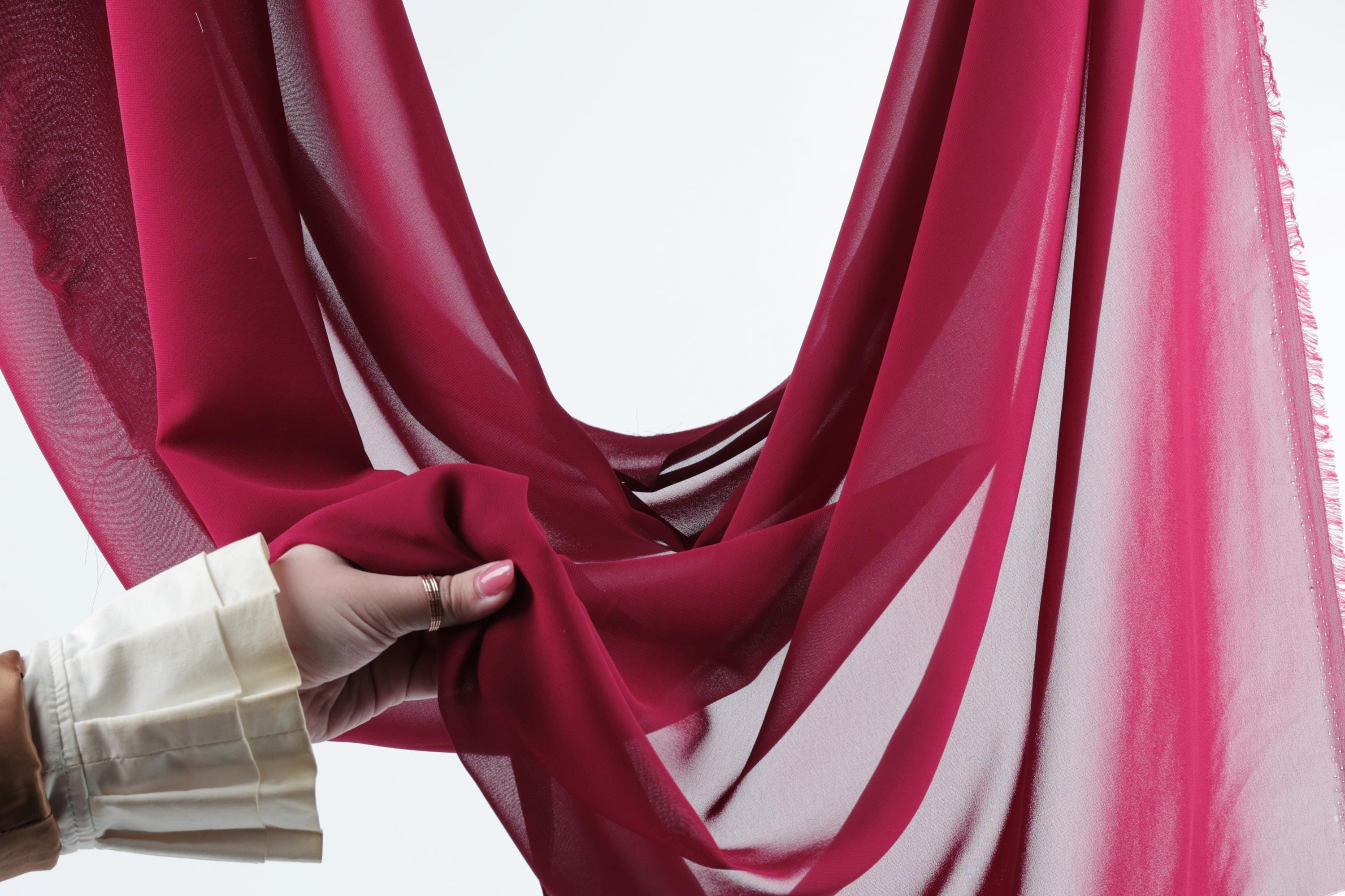 A hand is holding a red fabric, possibly a scarf or a garment, against a white background.