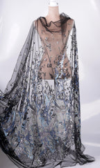 A mannequin wearing a long, flowing black and silver sequined cape or shawl.