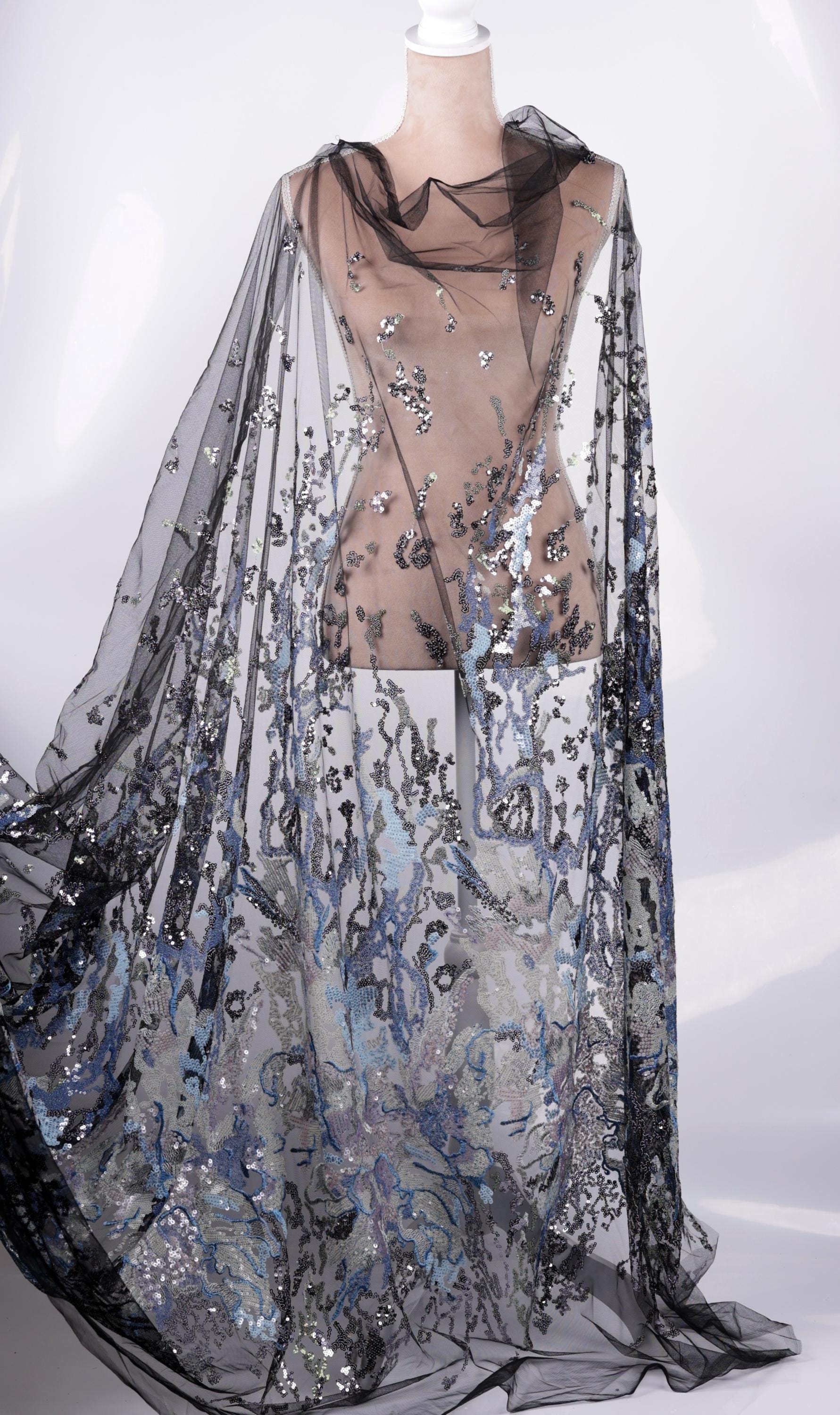 A mannequin wearing a long, flowing black and silver sequined cape or shawl.