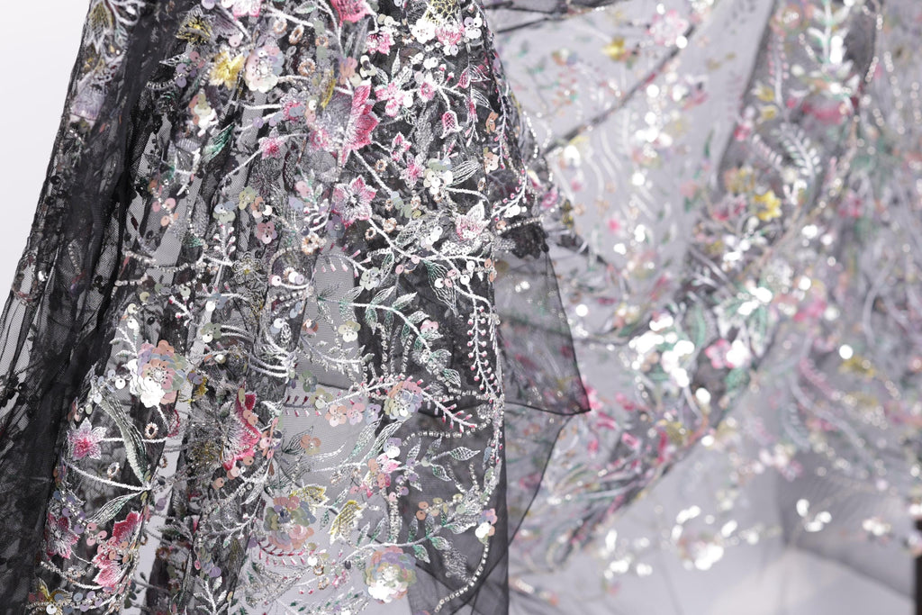 a close-up view of a delicate, intricately embroidered fabric with a floral pattern. The fabric appears to be a blend of black and white, with the black fabric adorned with a variety of colorful floral designs. The close-up perspective allows for a detailed examination of the fabric's texture and the intricate embroidery work.