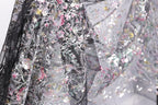a close-up view of a delicate, intricately embroidered fabric with a floral pattern. The fabric appears to be a blend of black and white, with the black fabric adorned with a variety of colorful floral designs. The close-up perspective allows for a detailed examination of the fabric's texture and the intricate embroidery work.