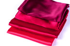 A stack of three red satin fabric pieces, with the topmost piece being the largest and the two smaller pieces being slightly smaller in size.