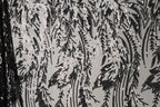 a close-up view of a black and white patterned fabric with a repeating design of black and white sequins or beads. The pattern appears to be a floral or leaf-like design, with the sequins or beads arranged in a way that creates a sense of movement and texture. The fabric has a textured surface, and the black and white color scheme adds a classic and timeless aesthetic to the design.