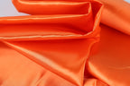 The image is a close-up of a bright orange fabric, possibly silk or satin, with a shiny and smooth texture.
