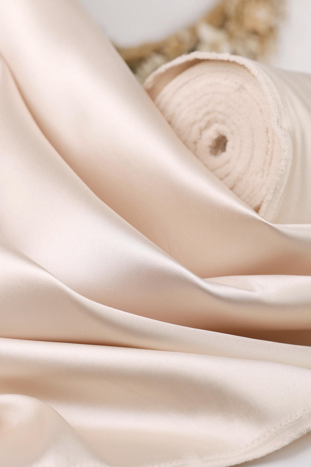 A close-up image of a soft, light pink satin fabric, possibly silk or satin, with a curled and folded appearance.